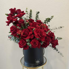 Red roses arranged in a black hat box with eucalyptus accents