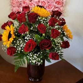 Bouquet of red roses and yellow sunflowers in a dark glass vase