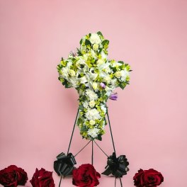 Cross-shaped floral tribute on a stand with white and green flowers and red roses below