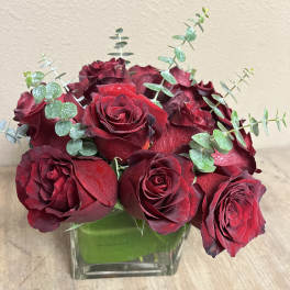 Red roses arranged in a square glass vase with eucalyptus stems