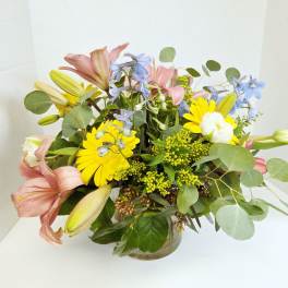 Mixed bouquet of lilies, daisies, and blue flowers in a glass vase