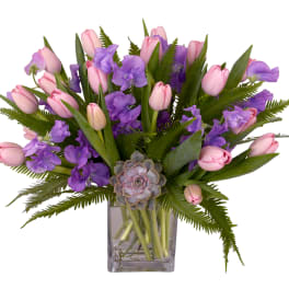 Pink tulips and purple flowers arranged in a clear glass vase
