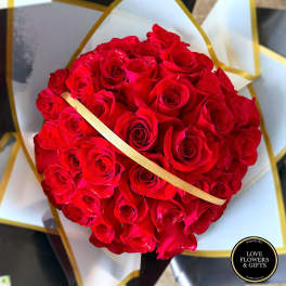 Round bouquet of tightly clustered red roses wrapped in white and black paper with gold accents.