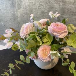 Blush pink flowers arranged in a white vase with trailing greenery