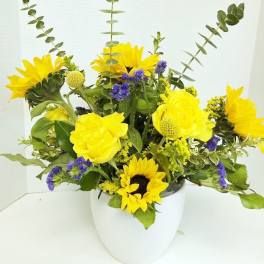 Yellow sunflowers and purple filler flowers in a white vase