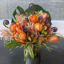Orange tulips and protea in a glass vase with curled accents