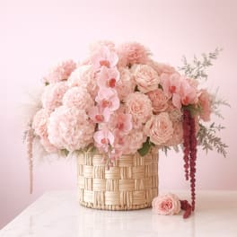 Blush pink floral arrangement in a woven basket with orchids and roses