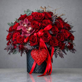 Red rose arrangement in a dark vase with a ribbon and heart decoration