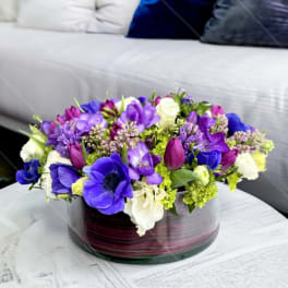 Purple and white floral arrangement in a round glass vase