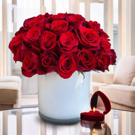 Red roses arranged in a white vase beside a small red candle box