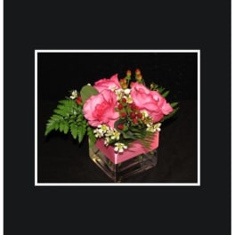 Pink roses arranged in a square glass vase with greenery