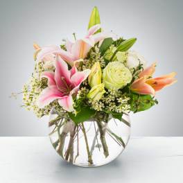Pink lilies and pale roses arranged in a clear glass vase