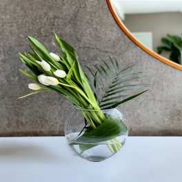 White tulips in a round glass vase with palm leaves