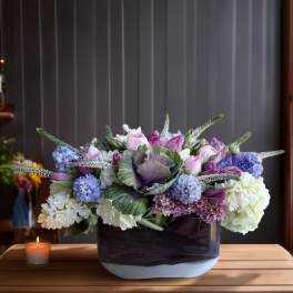 Lavender and white floral arrangement in a low rectangular vase beside a candle