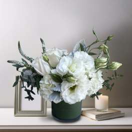 White floral arrangement in a green vase with a lit candle beside it
