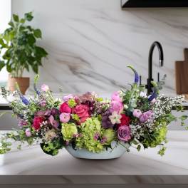 Low floral centerpiece with pink, purple, and green blooms in a shallow bowl