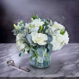 White floral bouquet in a clear glass vase beside a decorative key