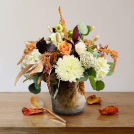 Mixed floral arrangement in a glass vase with an orange rose and white blooms