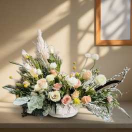 Low floral arrangement of pastel roses and white blooms in a white container