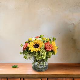 Bouquet of sunflowers, roses, and hydrangeas in a glass vase
