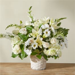 White floral arrangement in a woven basket with daisies and lilies