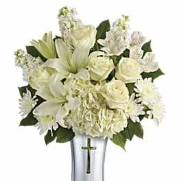 White lilies, roses, and daisies arranged in a silver vase with a cross
