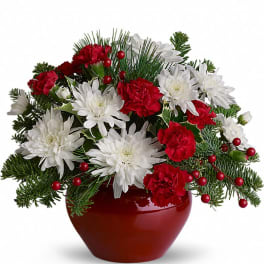 Red and white flowers arranged in a red vase with evergreen accents