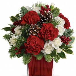 Red and white floral arrangement in a clear square vase with pinecones
