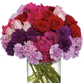Bouquet of red roses, pink hydrangeas, and purple carnations in a clear glass vase