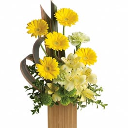 Yellow gerbera daisies and pale flowers in a tall wooden vase