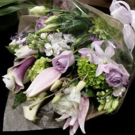 Bouquet of lavender, white, and green flowers wrapped in clear plastic with a white bow