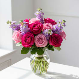 Pink and magenta roses with lavender flowers in a glass vase