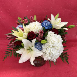 Bouquet of white lilies, red roses, and white hydrangeas in a glass vase