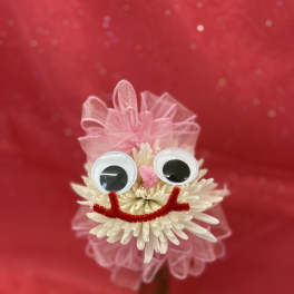White flower with googly eyes and pink ribbon on a red background