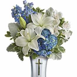White lilies and blue flowers arranged in a silver vase with a cross