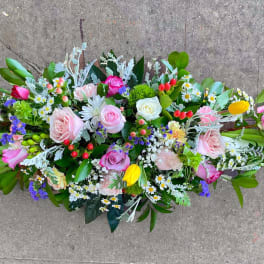 Low elongated arrangement of pink roses, yellow tulips, and mixed spring flowers