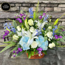 Basket arrangement of white lilies and roses with blue hydrangeas and purple blooms