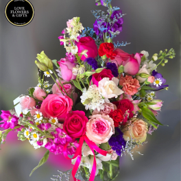 Mixed bouquet of pink roses, carnations, and daisies in a clear glass vase with bright pink ribbon.