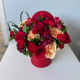 Red and peach roses arranged in a round red box