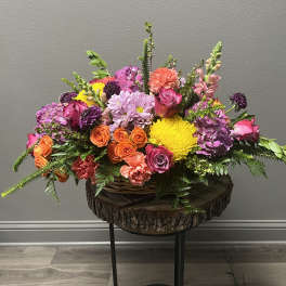 Colorful mixed flower arrangement in a wicker basket on a wood slab stand