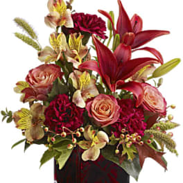 Bouquet of red lilies, pink roses, and burgundy flowers in a glass vase