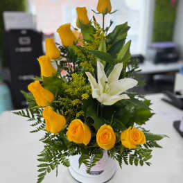 Yellow roses and a white lily arranged in a white vase