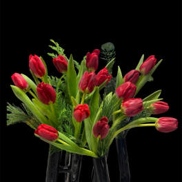 Red tulips arranged in a clear glass vase with greenery