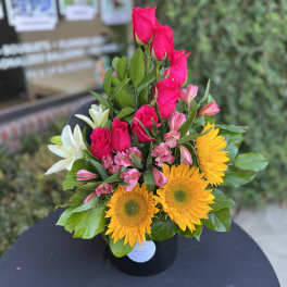 Bouquet of hot pink roses, yellow sunflowers, and white lilies in a black vase