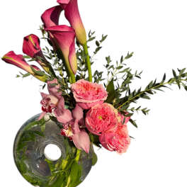 Pink calla lilies and roses arranged in a round glass vase