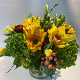 Yellow mixed bouquet in a clear glass vase with sunflowers and orchids