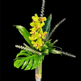 Yellow orchids in a tall glass vase with large tropical leaves