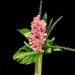 Pink orchids in a tall glass vase with large tropical leaves