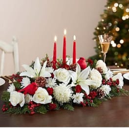 Holiday centerpiece with white flowers, red candles, and pinecones on a table