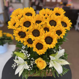 Basket arrangement of yellow sunflowers, white lilies, and a yellow rose